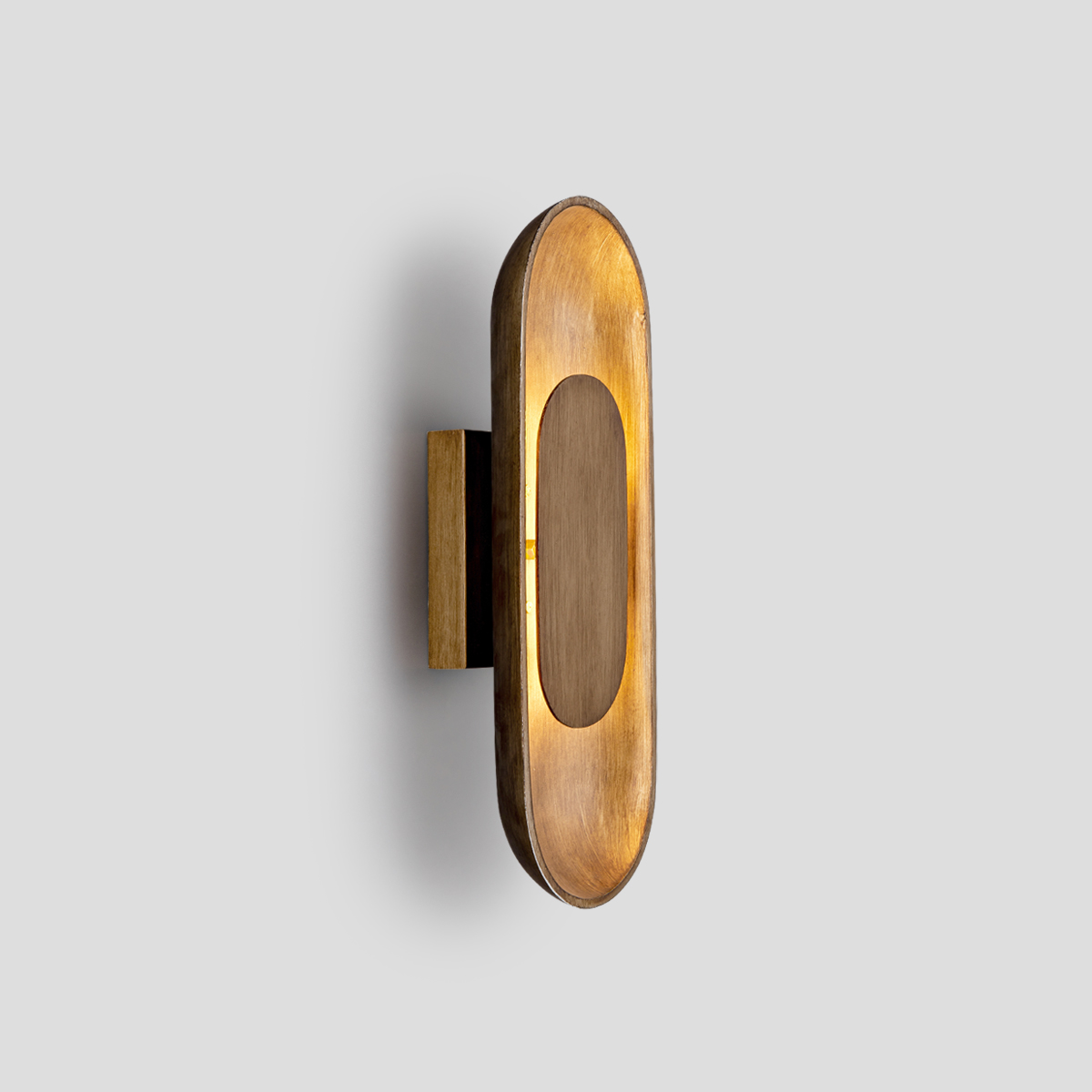 Modern Oval LED Wall Sconce 1 Modern oval LED wall sconce in brushed brass on a deep blue entryway wall next to a round mirror and potted plant.