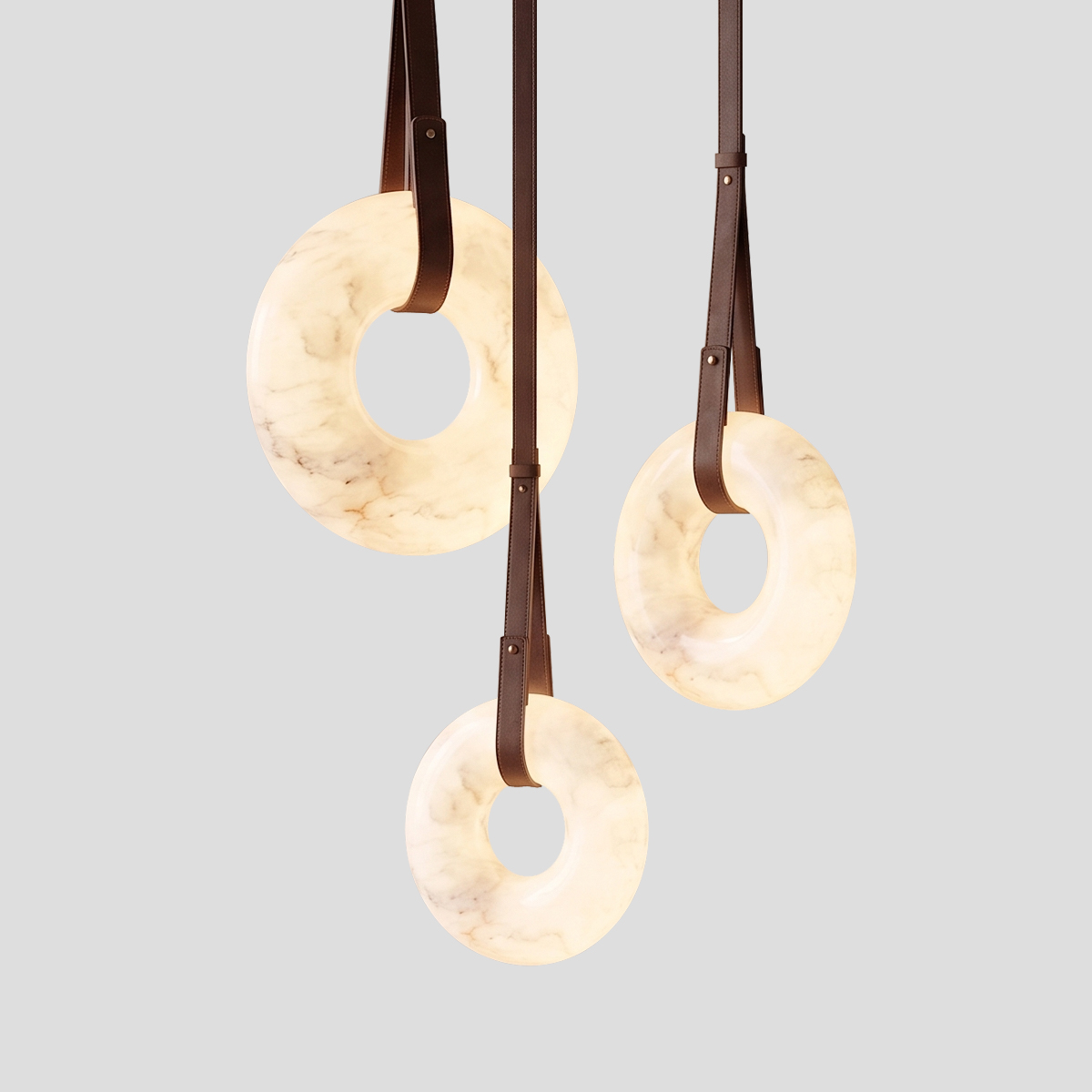 Alabaster Ring Pendant Light 1 Alt Text: Three illuminated alabaster ring pendant lights suspended by brown leather straps with brass hardware against a light grey background.
