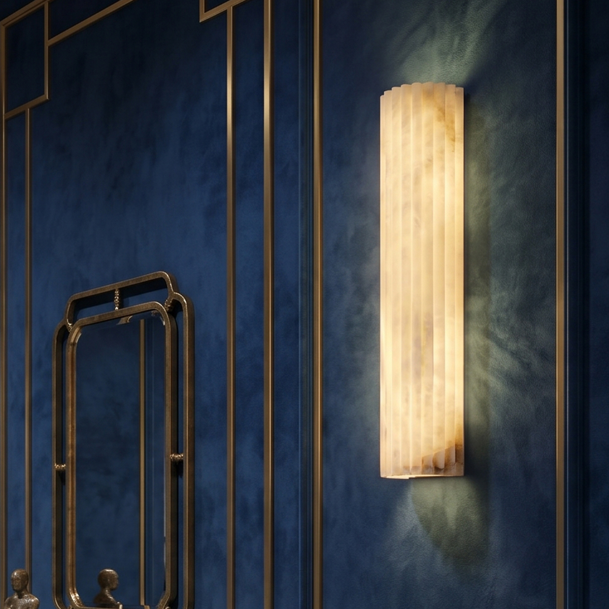 Valerie Fluted Alabaster Wall Sconce 3 Luxury modern alabaster wall lamp on a textured deep blue wall with gold trim next to a vanity mirror.
